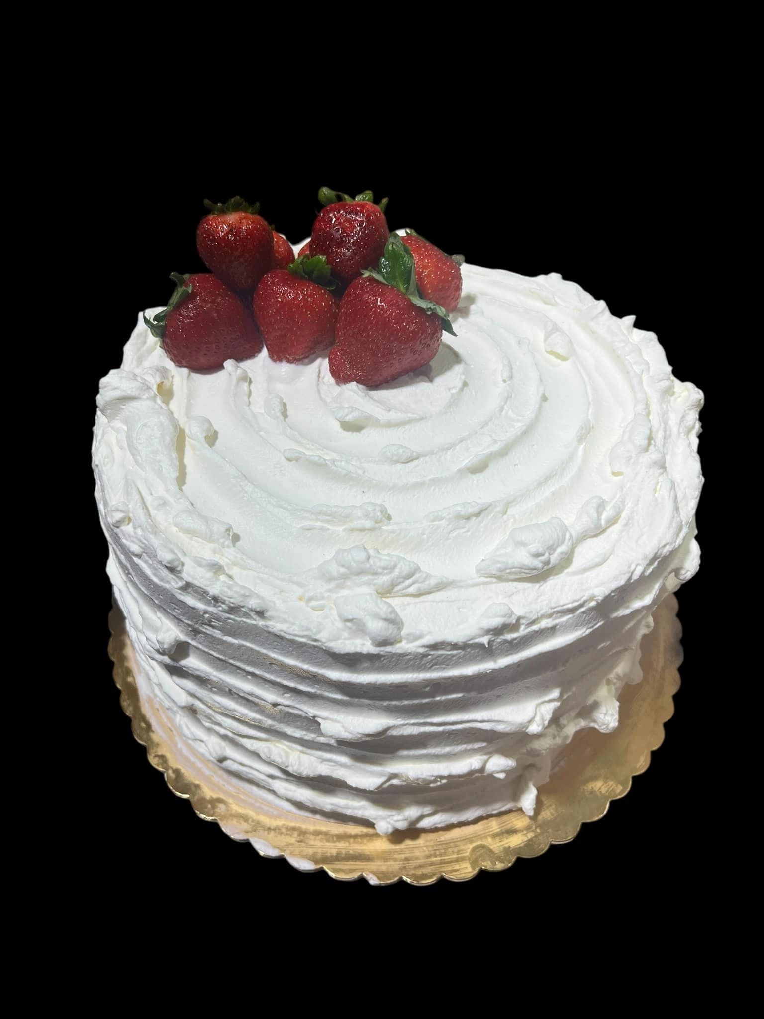 Round white frosted cake topped with fresh strawberries on a gold base.