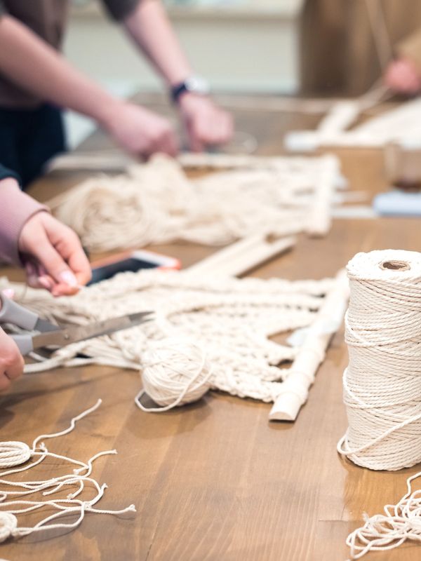 a group of people gathered around a rectangular table, each working on a macrame project