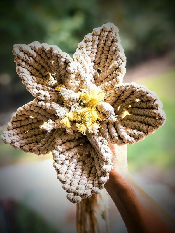 a hand holding up a big macrame flower that has 5 pedals and yellow fuzzy pistil