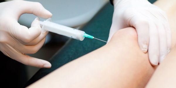 Gloved hands administering an injection into a knee.