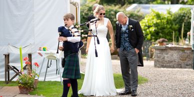 Married couple with young person playing bagpipes outside marquee.