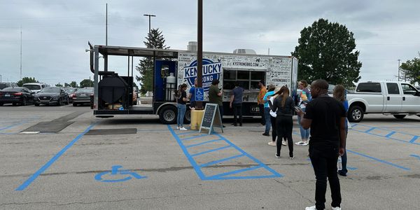 People waiting in line at a Kentucky BBQ food truck in a parking lot.