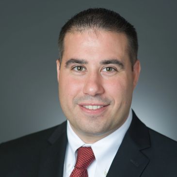 Professional headshot of a man in a suit and red tie.