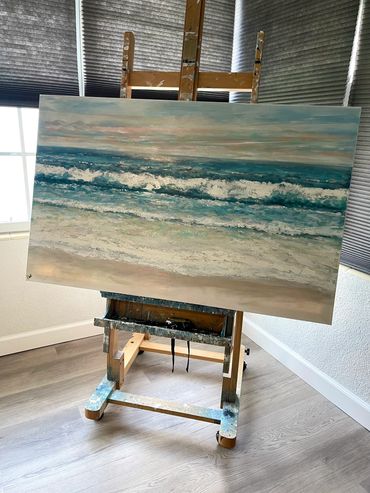 A serene seascape painting on an easel in a bright room.