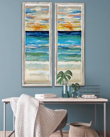 Coastal-themed diptych paintings above a minimalist desk with plants and a cozy chair.