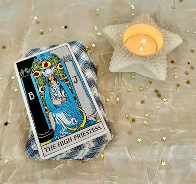 Tarot card 'The High Priestess' next to a lit star-shaped candle.