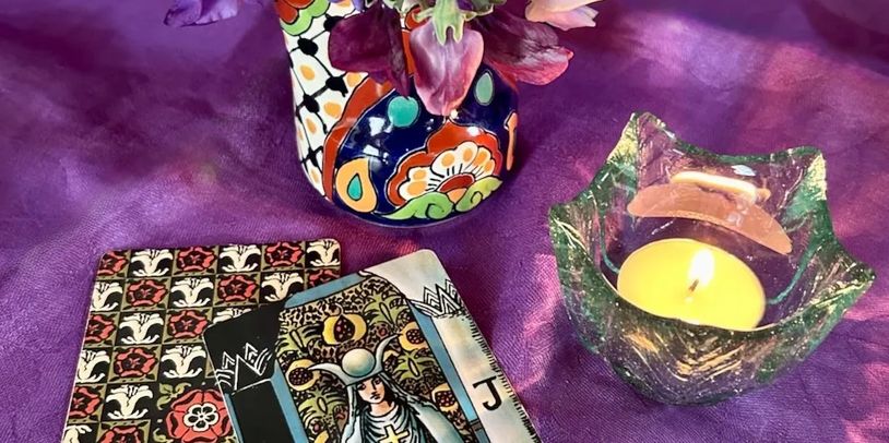 tarot cards on a purple table cloth with a tea light candle and a small jug with flowers.