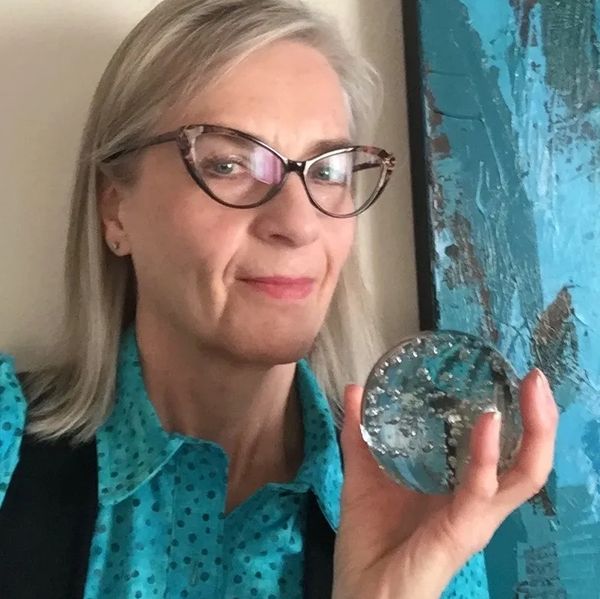 Kim wearing black glasses, a teal polka dot shirt and black vest holding a glass ball paper