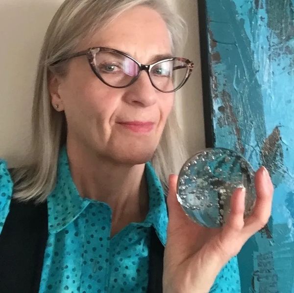 A woman wearing glasses and a blue with shirt and black vest holding a crystal ball