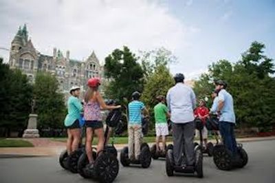 Group of people riding Segways in a park near historic buildings.