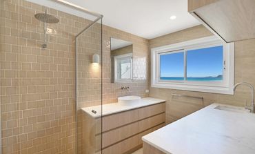 Modern bathroom with glass shower and beige tiles.