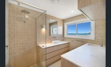 Modern bathroom with glass shower and beige tiles.