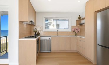 Bright modern kitchen with light wood cabinets and ocean view balcony.