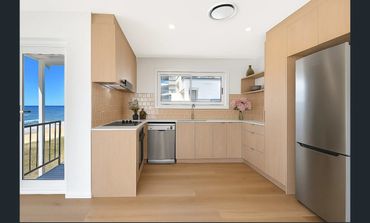 Bright modern kitchen with light wood cabinets and ocean view balcony.