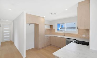 Modern kitchen with light wood cabinets and white marble countertop.
