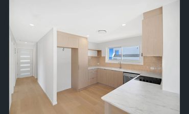 Modern kitchen with light wood cabinets and white marble countertop.