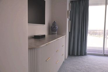 Modern bedroom corner with a stylish dresser, TV, and large window.