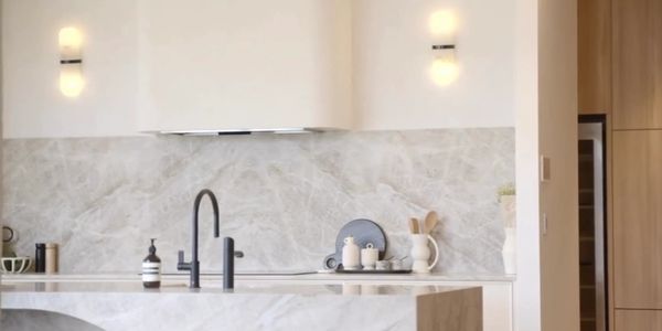 Modern kitchen with marble surfaces and black faucet under soft wall lights.