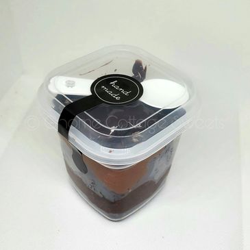 A clear plastic container with chocolate dessert and a spoon on top.