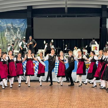 Group performing traditional Bavarian dance in festive attire on stage.