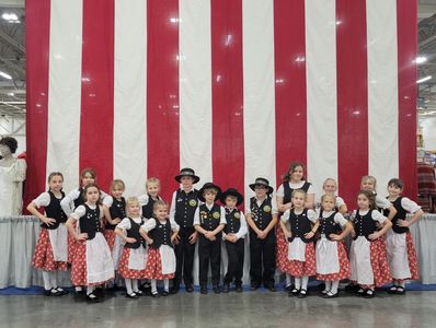 Children in traditional folk costumes posing in front of a large American flag.