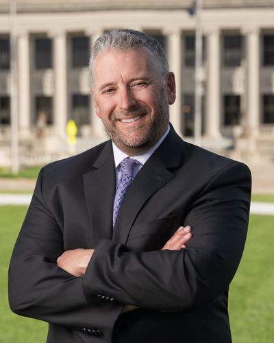 Confident man in suit smiling outdoors with arms crossed.