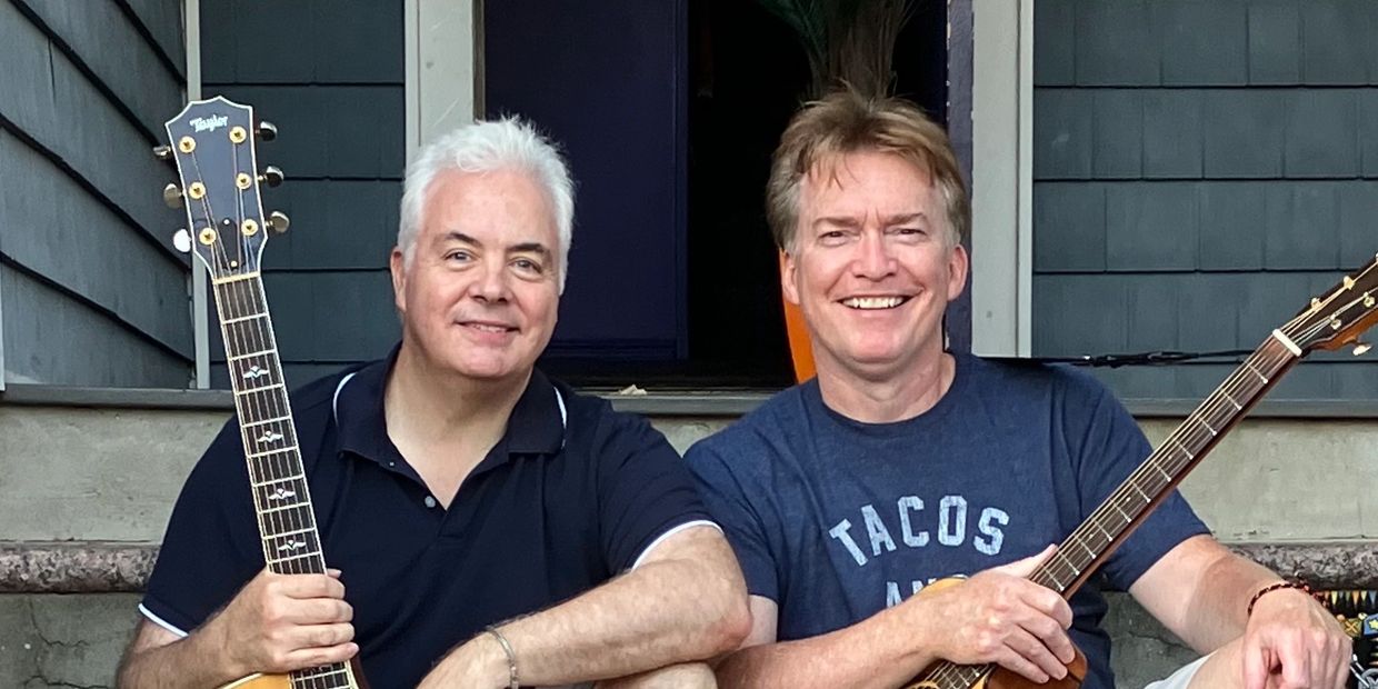 Two men sitting with guitars, smiling.