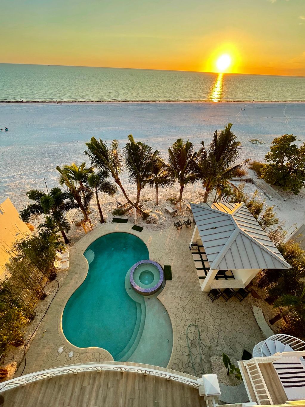 A serene beachside pool area at sunset with palm trees and a gazebo.
