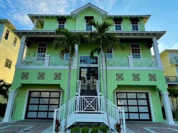 Bright green house with twin garages and palm trees at the entrance.