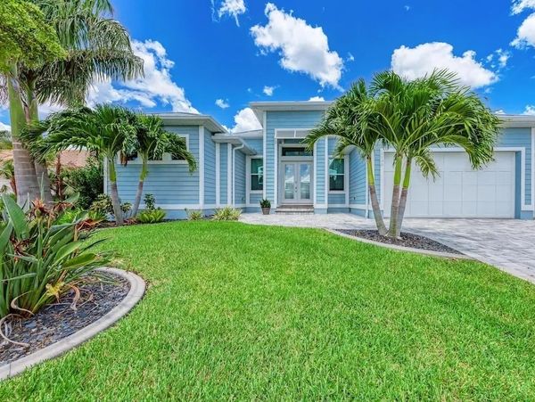 Modern blue house with lush green lawn and palm trees under a bright blue sky.