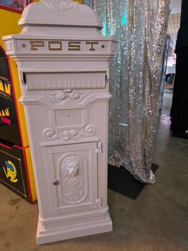 Vintage white post box with intricate designs and a lion emblem on a concrete floor.