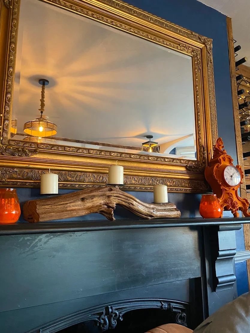 A cozy mantle with candles, rustic wood, and an ornate golden mirror reflecting warm lights.