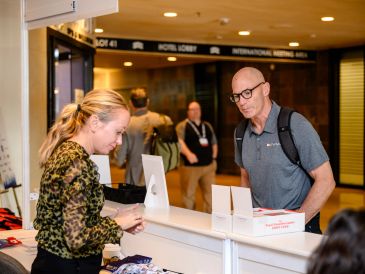 A man checking in at a reception desk while a woman assists.