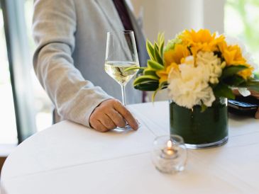 A person holding a glass of white wine at a table with flowers.