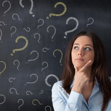 Woman thoughtfully looking at question marks on a chalkboard.