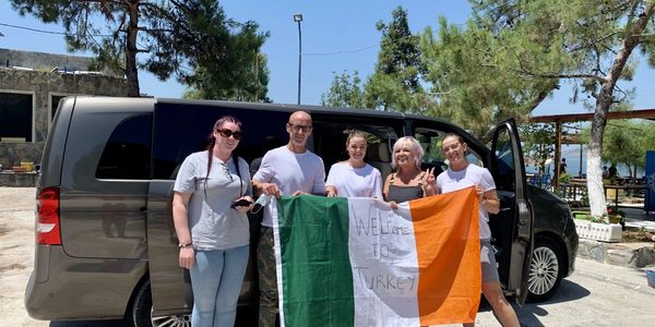 Five people holding an Irish flag in front of a black van outdoors.