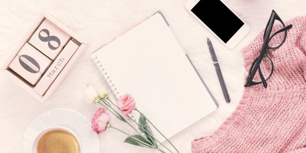 Soft, feminine flat-lay featuring an open lined journal, flowers, coffee, smartphone, glasses, and a