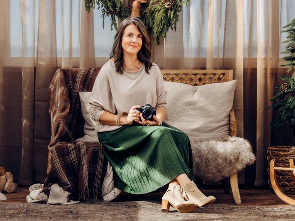 Woman sitting with a camera in a cozy, warmly lit room.
