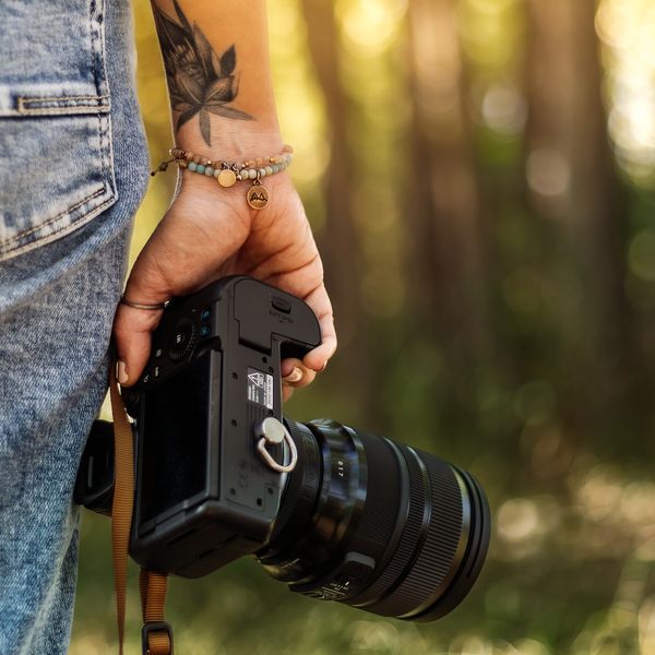 Person holding a camera with a wrist tattoo and bracelets.