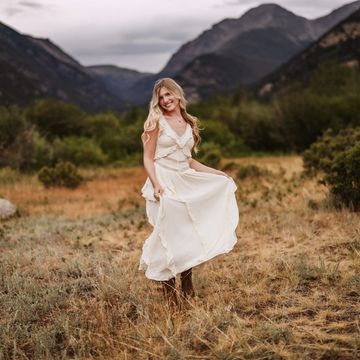 Smiling woman in a white dress with mountains in the background.