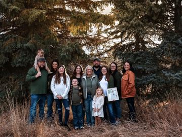 Large family group posing outdoors in front of tall trees.