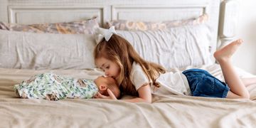 Young girl kissing a baby wrapped in a blanket.