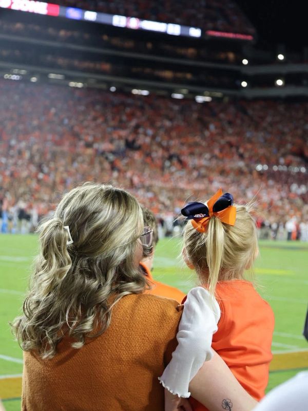 A woman and child watch a football game in a packed stadium at night.