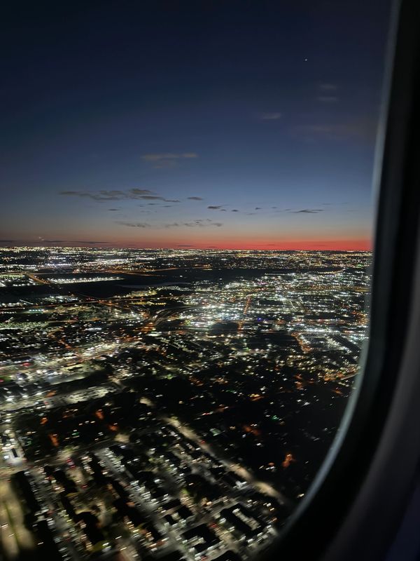 City lights glowing at dusk, viewed from an airplane window.
