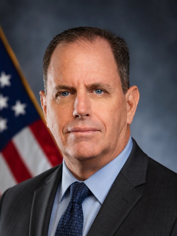 Man in suit with American flag background.