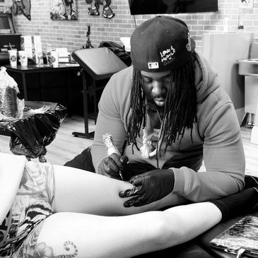 Tattoo artist working on a client's leg in a studio.