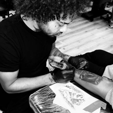 Tattoo artist working on a client's leg.