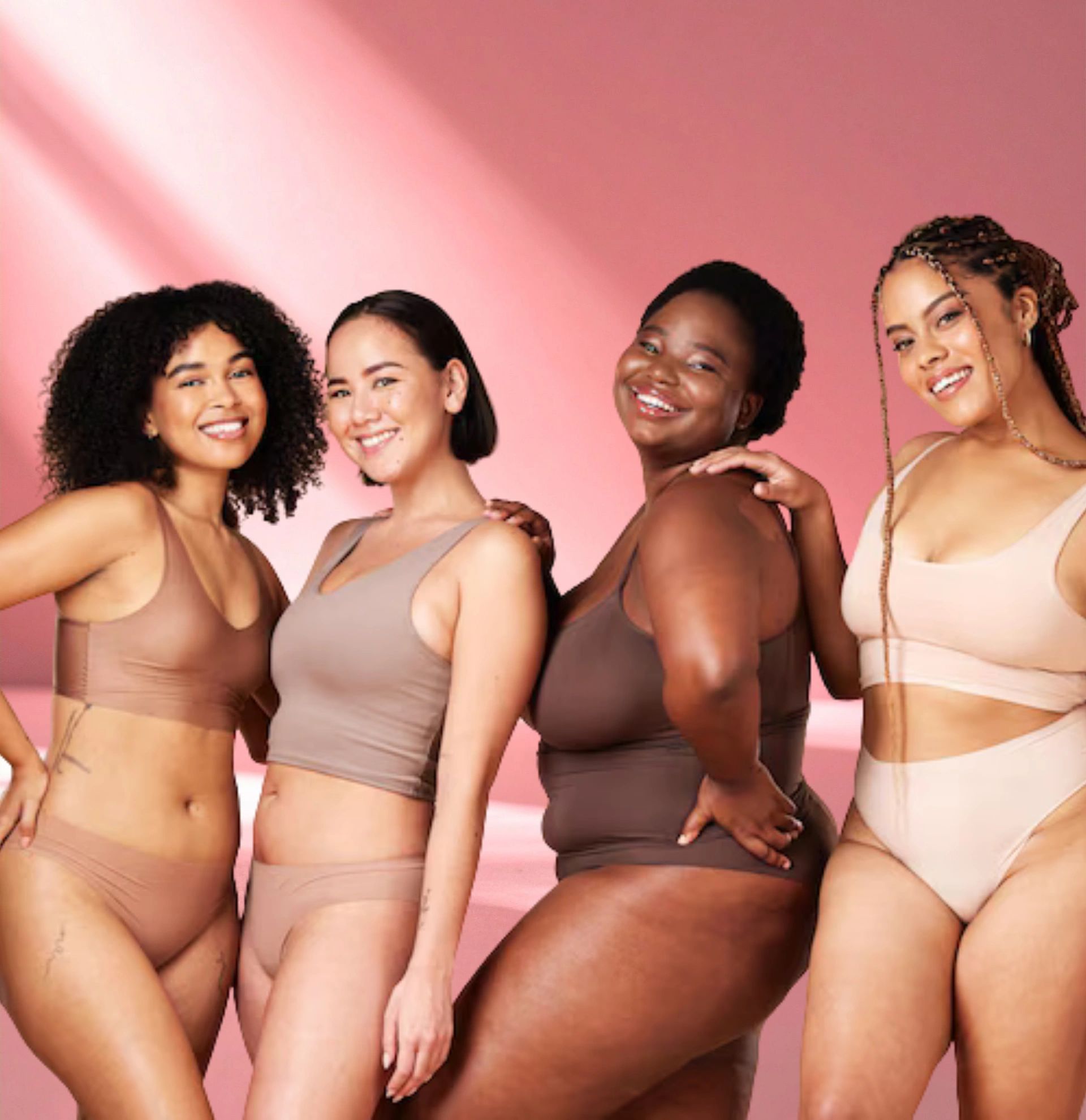 Four diverse women smiling in neutral-tone underwear.