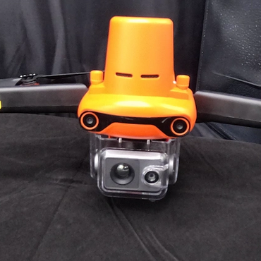 Orange and black drone with a mounted action camera on a black surface.