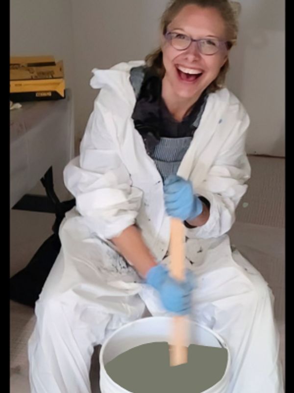 A joyful woman in protective clothing stirs a bucket with a wooden stick.